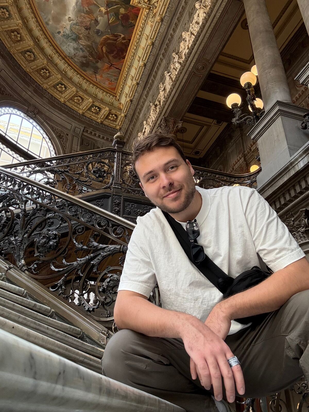 Elijah crouched on a marble staircase under an ornate painted ceiling