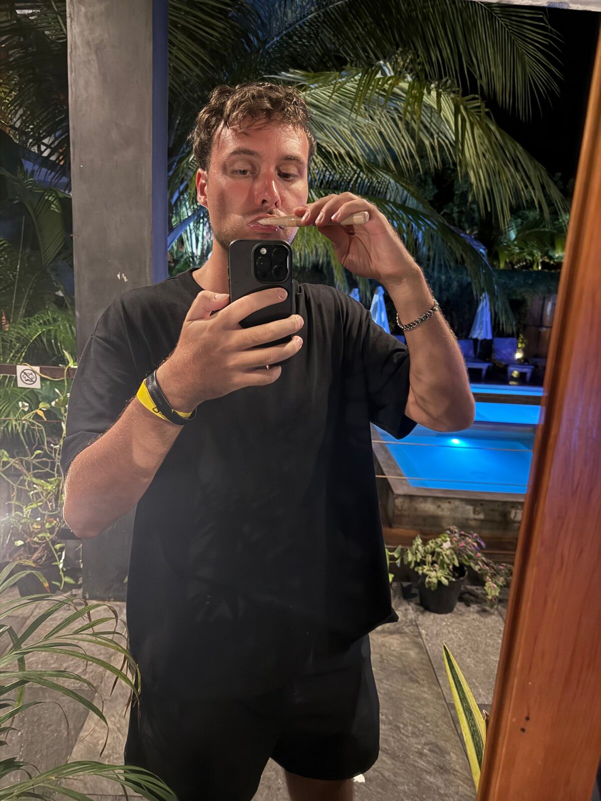 Mirror selfie at night by a lit pool and palm trees