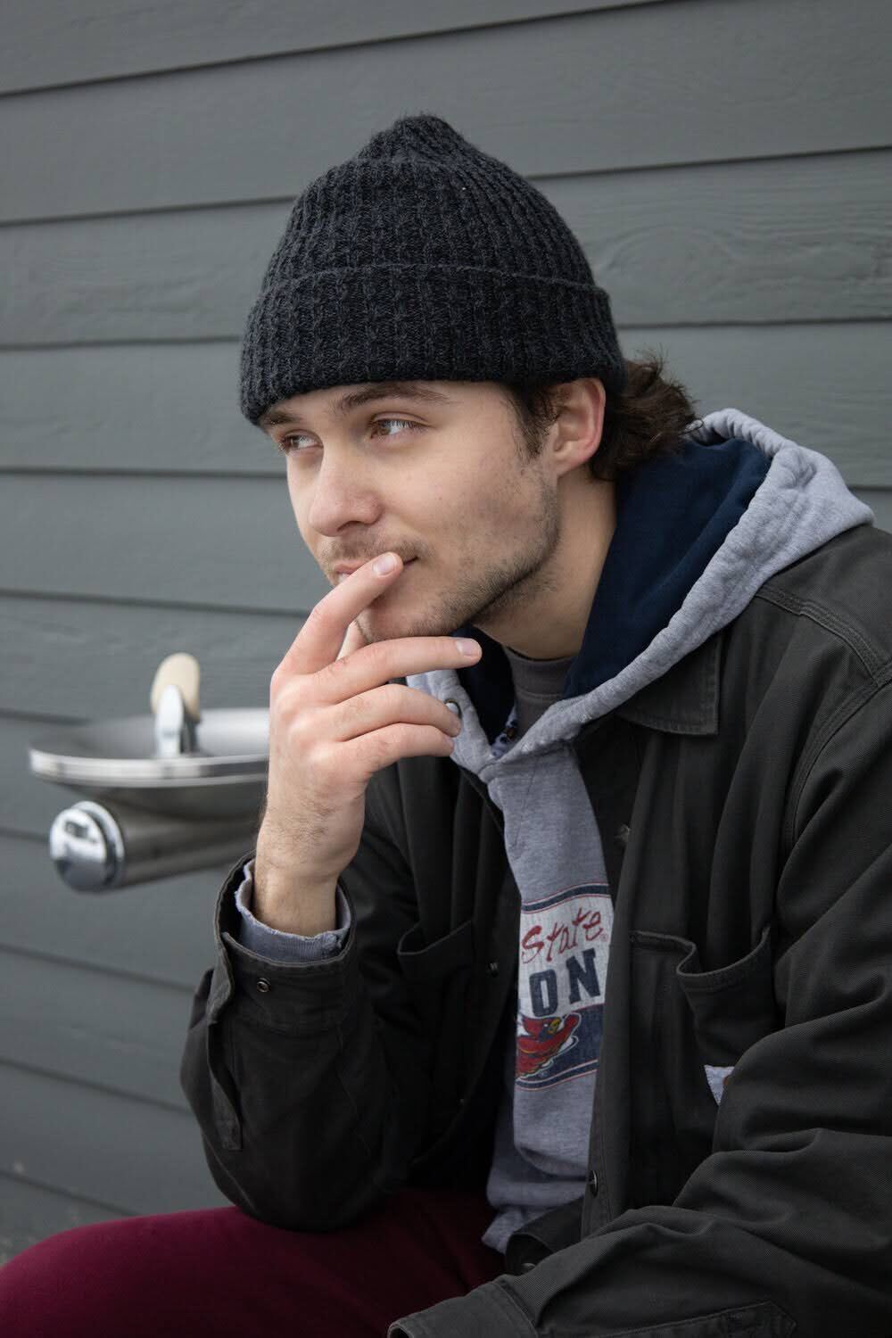 Elijah in a beanie and work jacket, looking off to the side