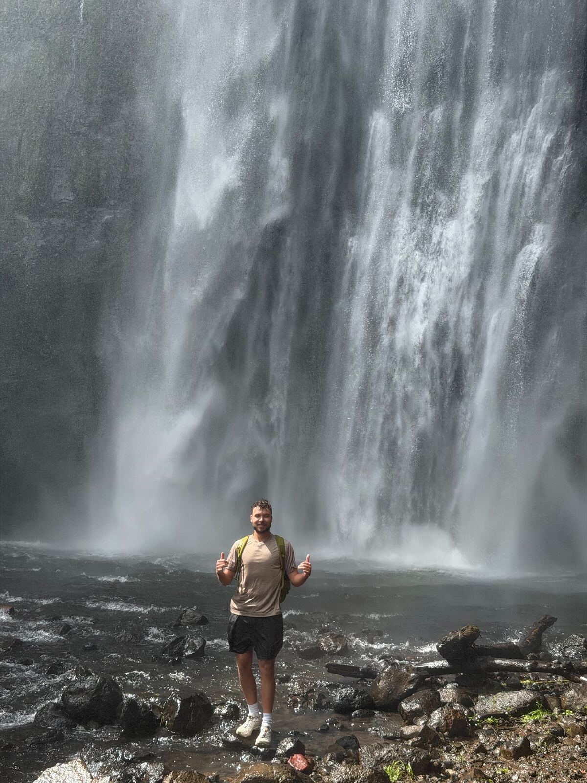 Elijah giving two thumbs up in front of a waterfall